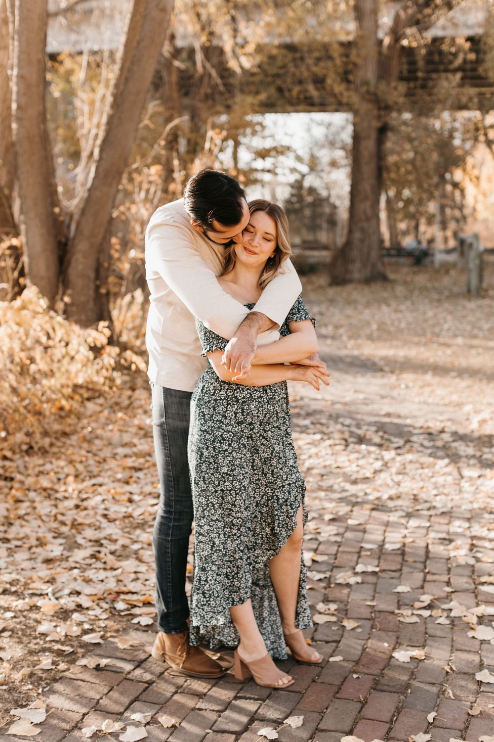 Couple sharing an intimate embrace on a brick path, surrounded by warm golden autumn leaves.