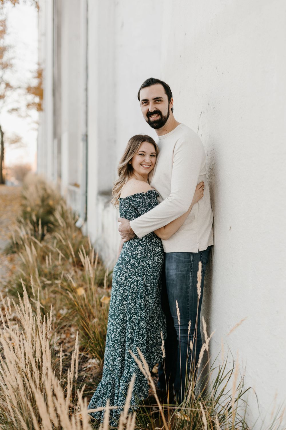 Happy couple embracing against a white wall surrounded by ornamental grasses in warm autumn light.