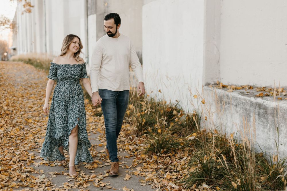 Couple walking hand in hand along a path lined with golden autumn leaves.