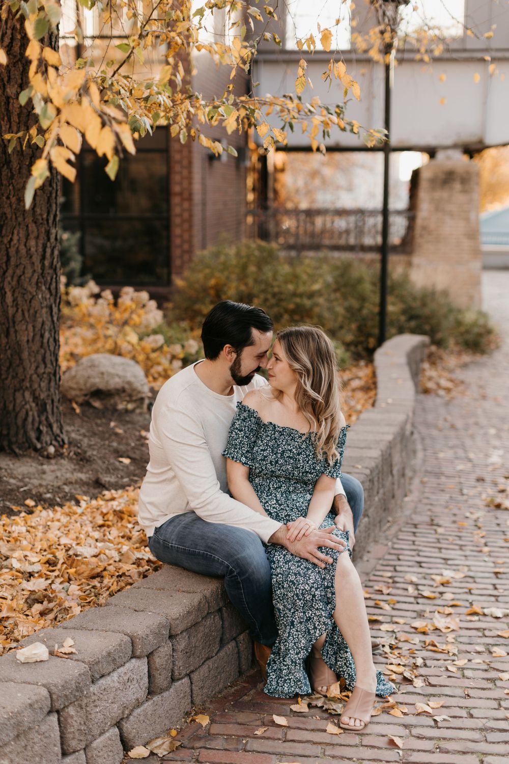 Romantic couple sharing a tender moment on a brick ledge in fall foliage.