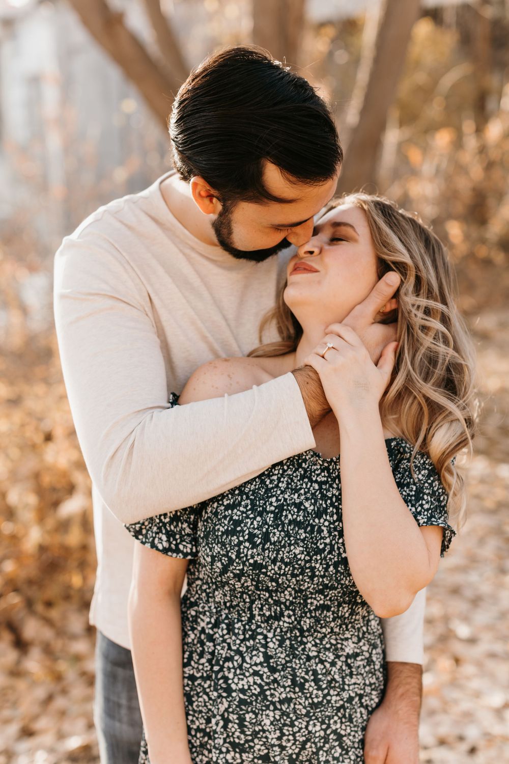 Couple sharing a tender kiss, man holding woman's face gently with engagement ring visible on hand.