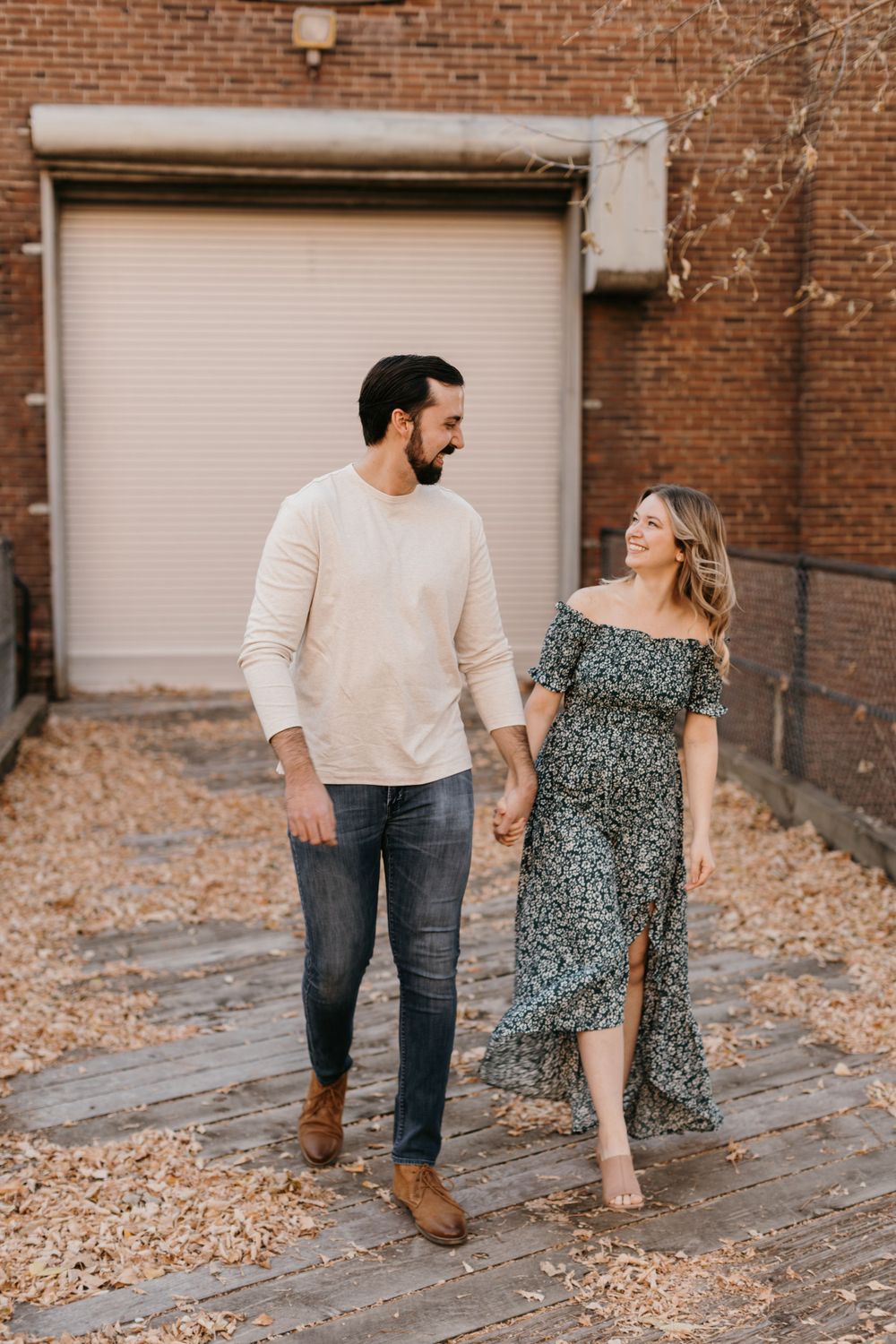 Smiling couple holding hands and strolling through a brick alley during their engagement session.