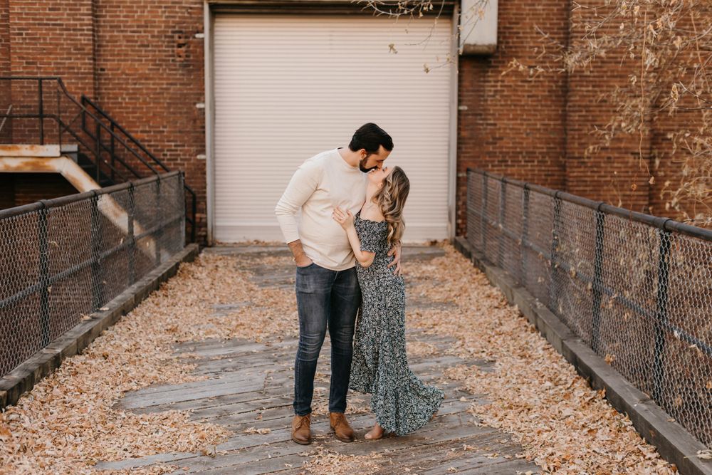 Couple sharing a tender kiss in a rustic brick alleyway during their engagement shoot.
