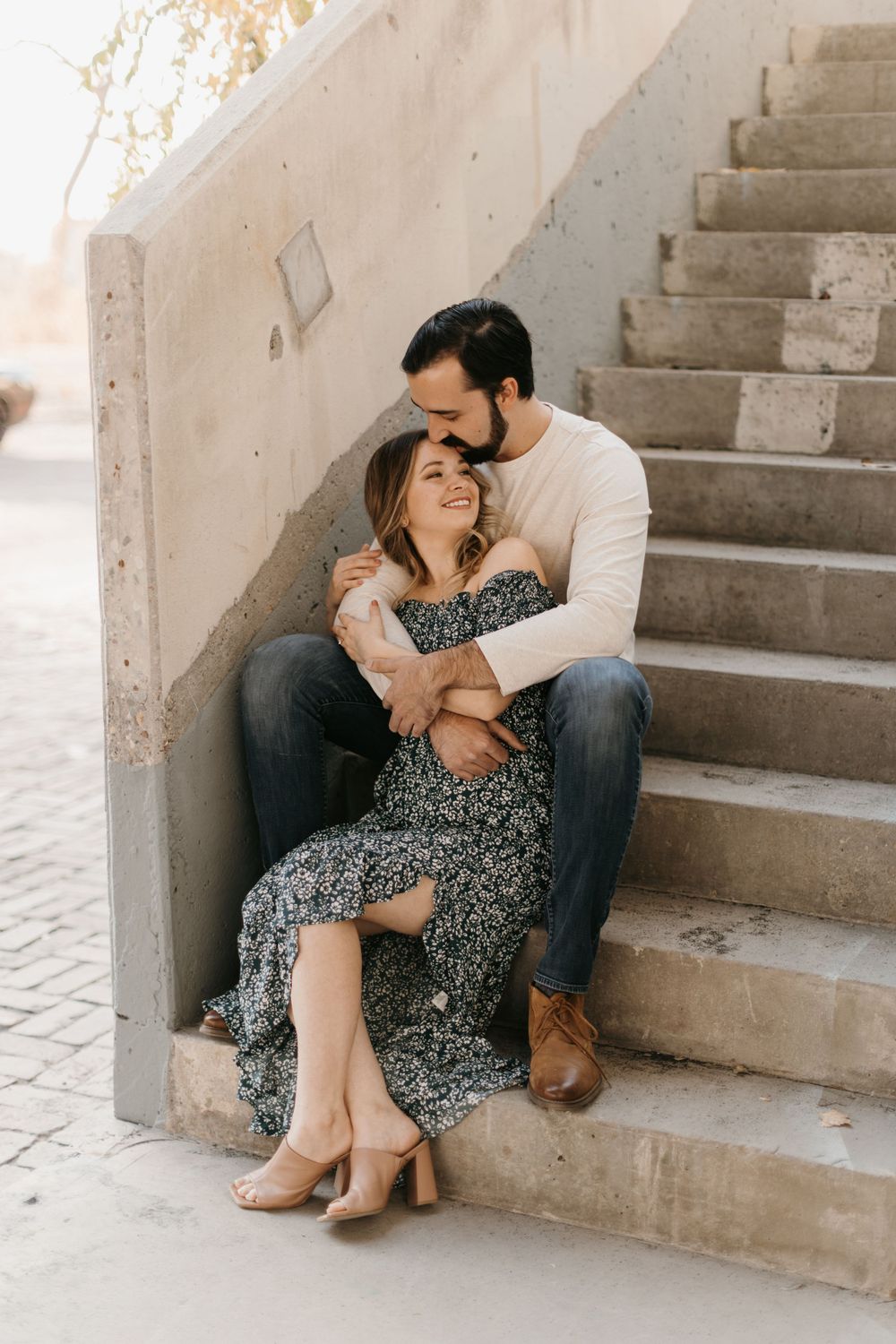 A couple shares a tender moment on concrete steps, man kissing womans head while embracing her.