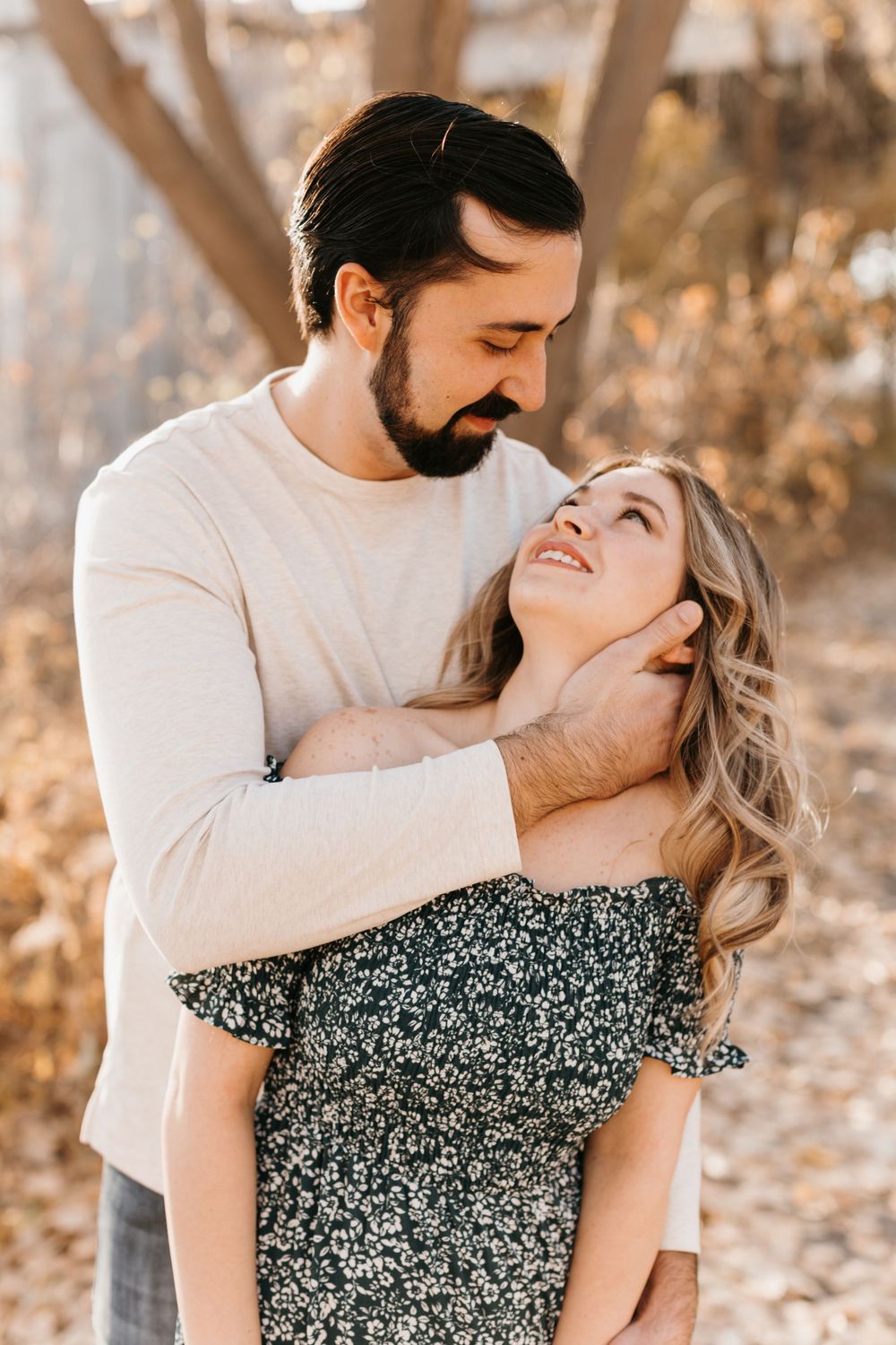 Romantic couple gazing at each other lovingly, man gently holding woman's face in autumn light.