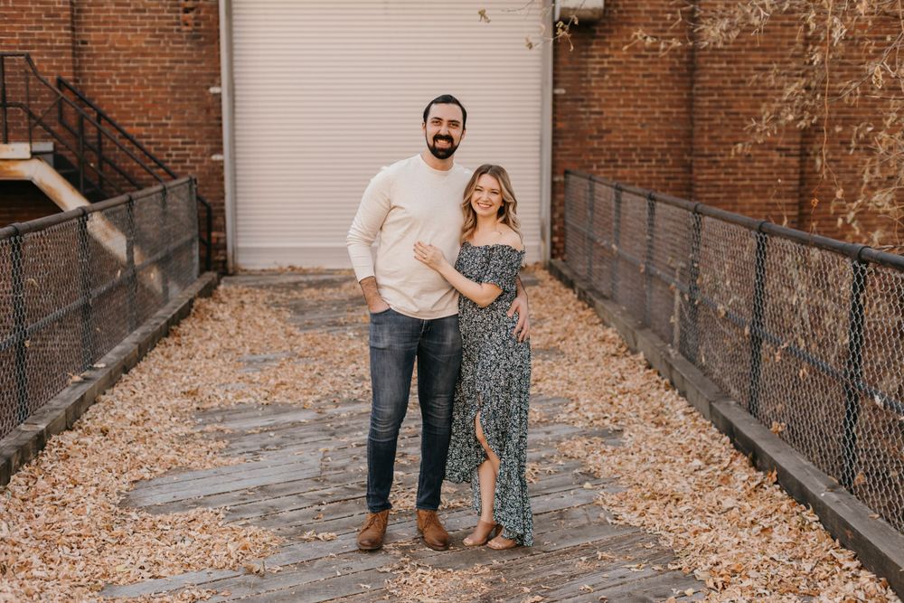 Happy couple standing close together in a leaf-covered brick alleyway during engagement photos.