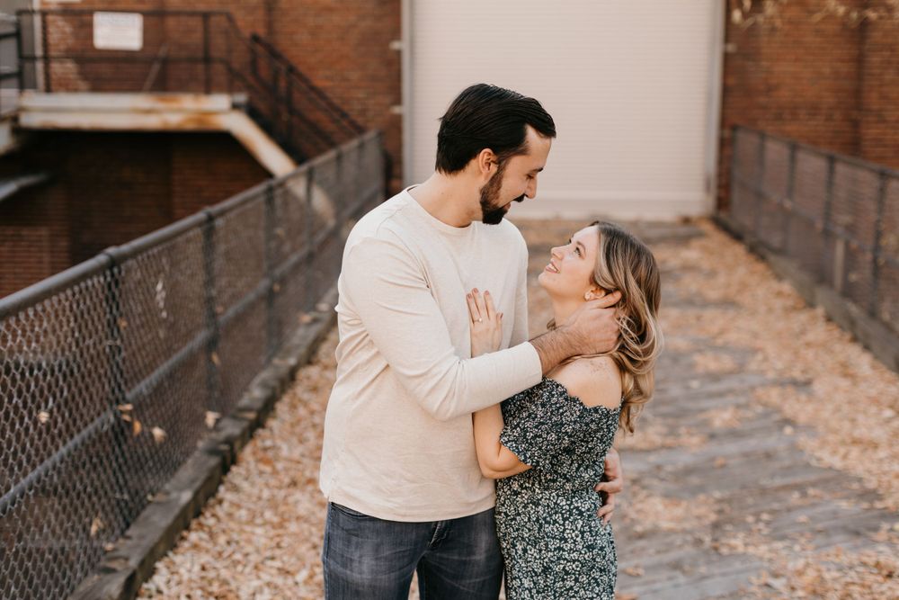 Romantic couple embracing and gazing at each other outdoors, man in cream sweater holding woman in floral dress.