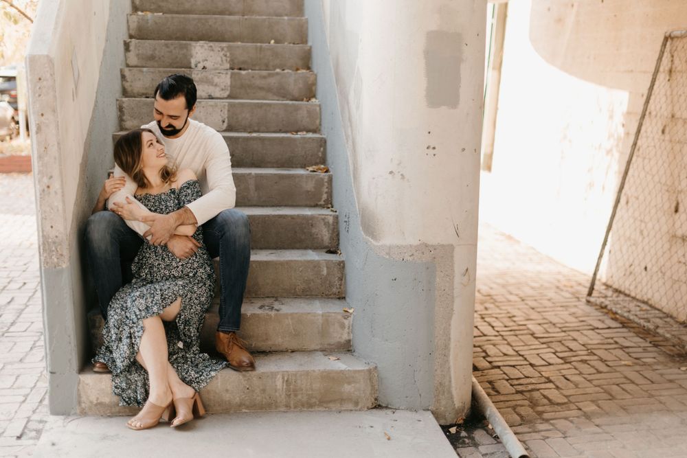 A couple shares an intimate embrace while seated on concrete stairs in an outdoor urban setting.