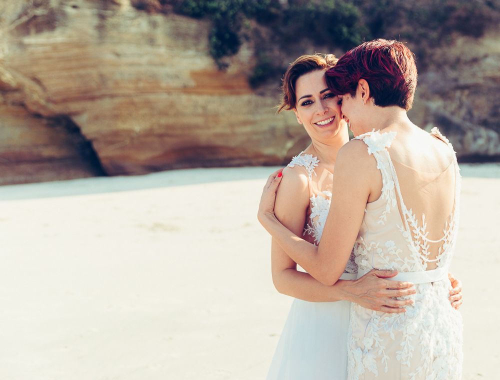 Intimate beach wedding portrait with coastal cliffs and natural lighting.