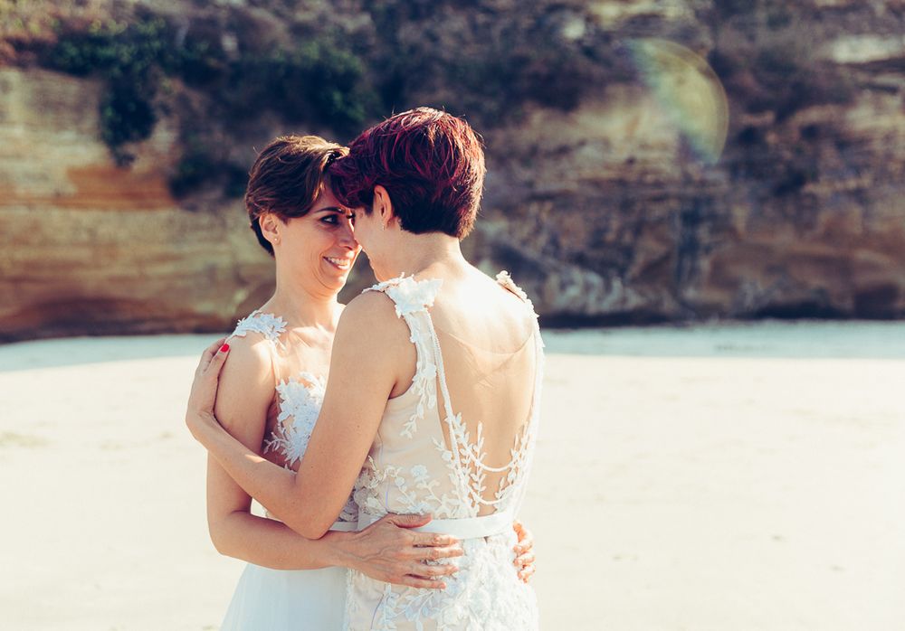 Romantic beach wedding photoshoot with rugged cliffs and coastline in background.