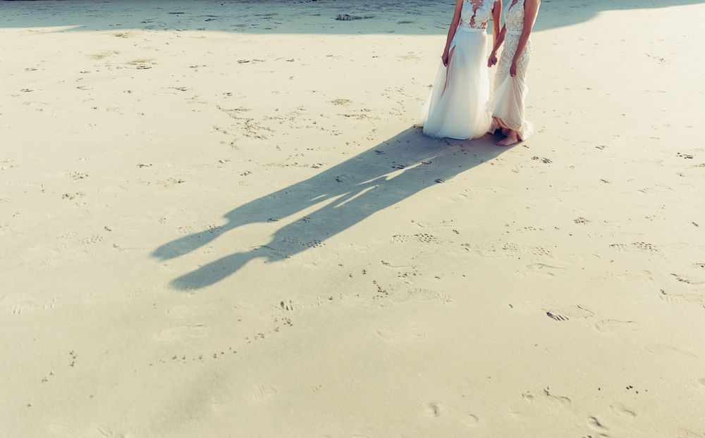Long shadows cast on sandy beach by figures in flowing white dresses.