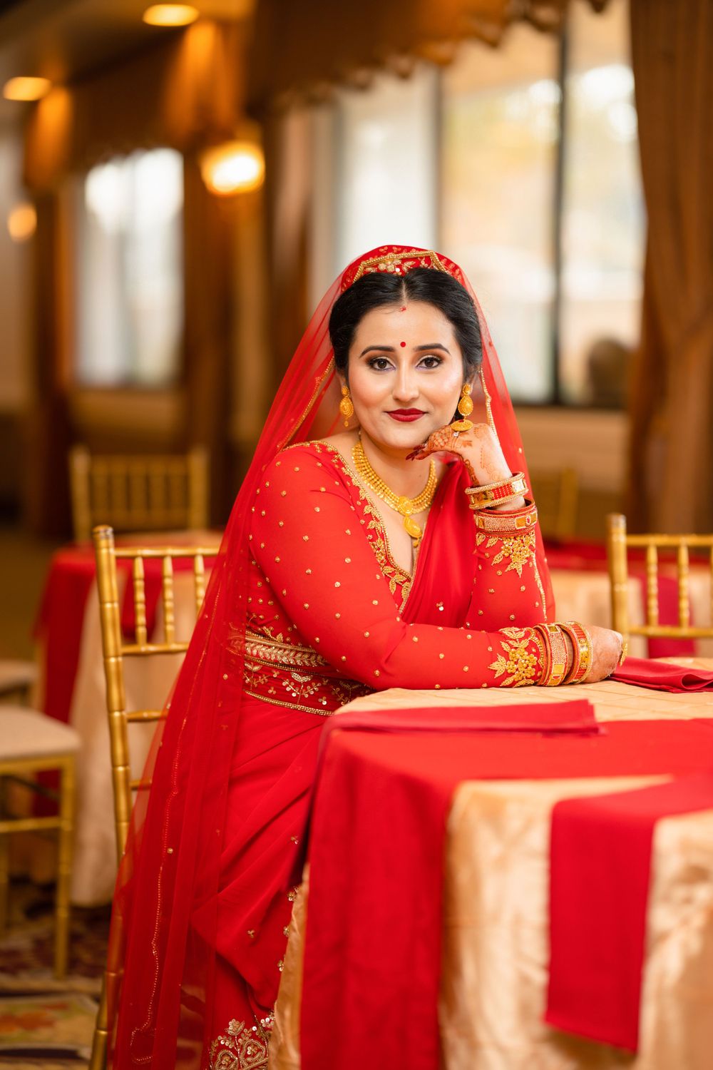 A bride in a traditional red Indian wedding sari poses elegantly at a decorated reception table.