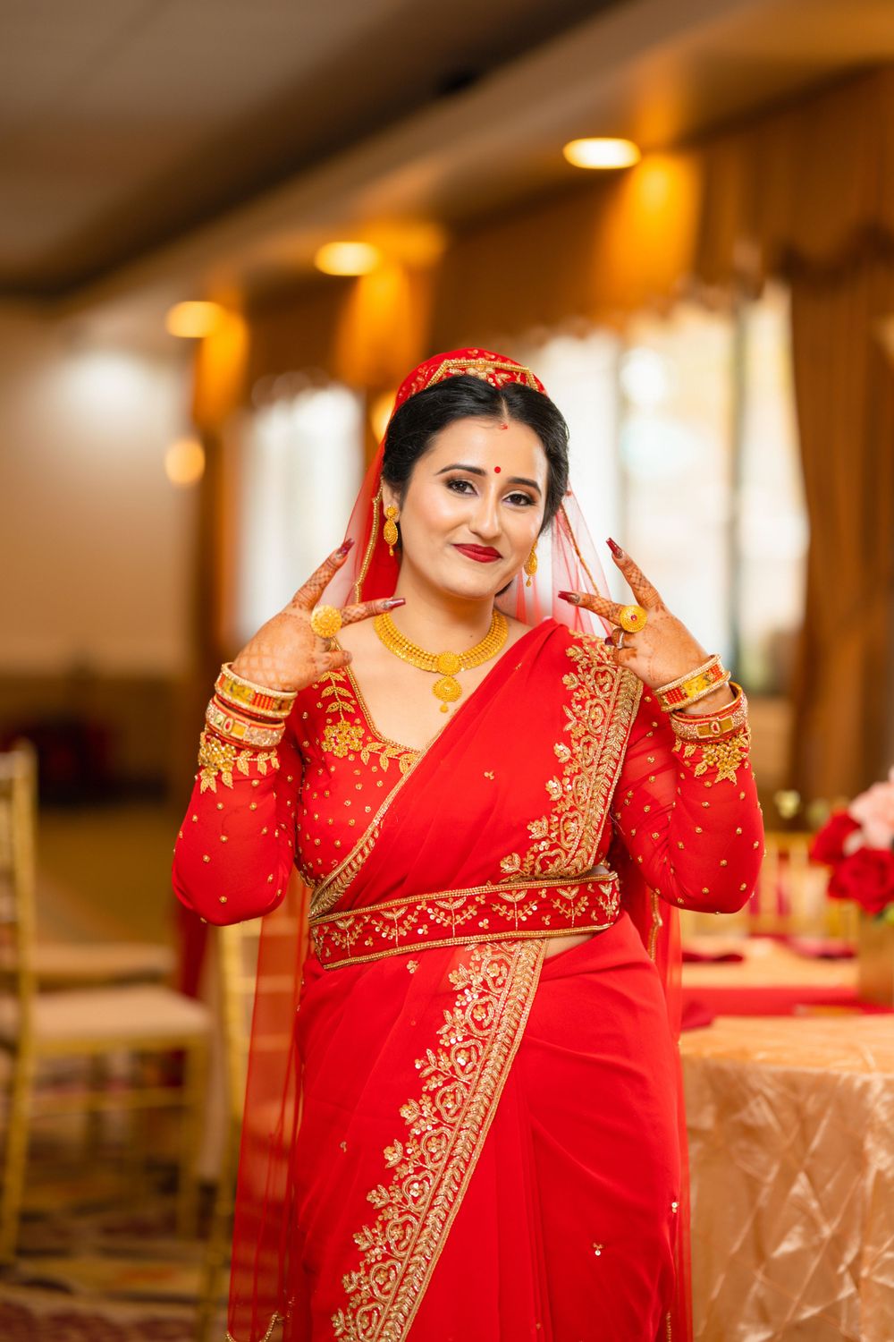 A bride in a vibrant red sari with gold embroidery poses gracefully at her wedding reception.