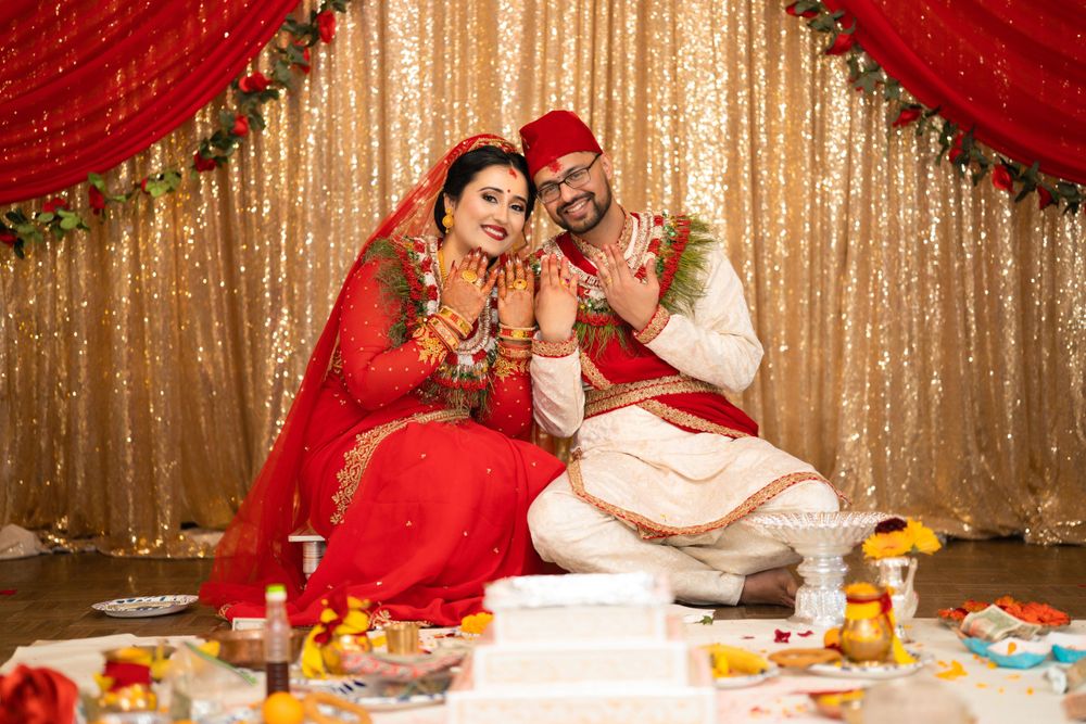 A newly married couple in traditional red wedding attire sits together with celebratory decorations.