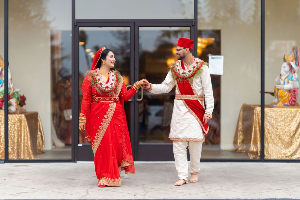 A couple in traditional red and white wedding attire dances joyfully outside their venue.