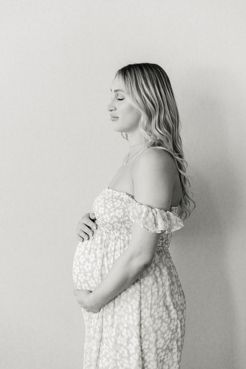 a black and white profile of a pregnant woman with eyes closed holding her bump against a neutral backdrop