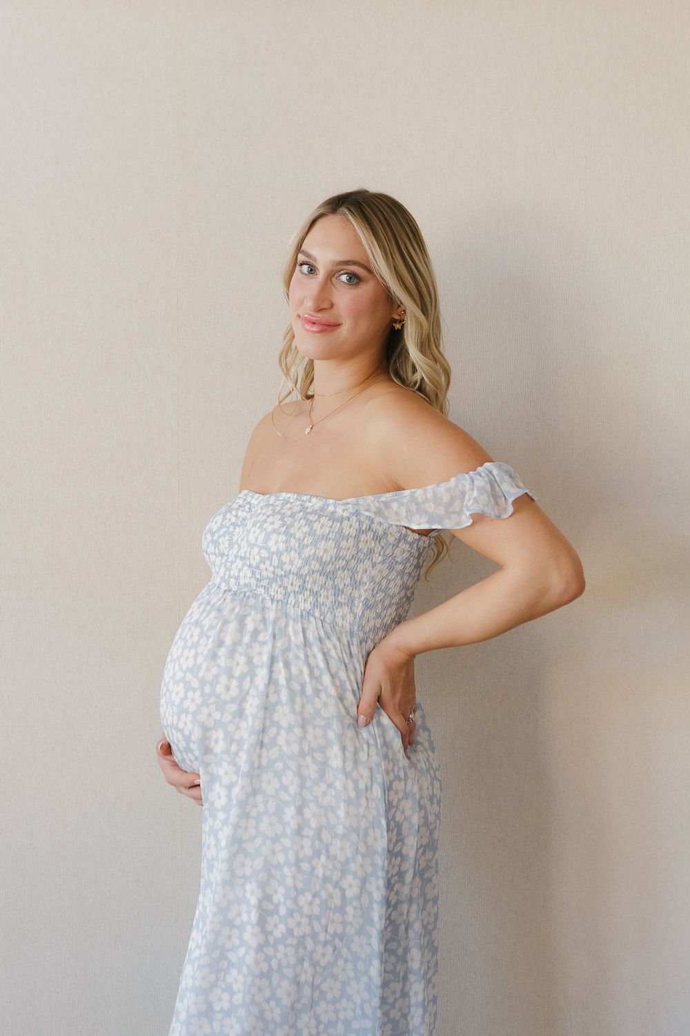 a semi profile view of a pregnant woman smiling while wearing a blue floral dress photo by Paula Ortiz NY Family Photos