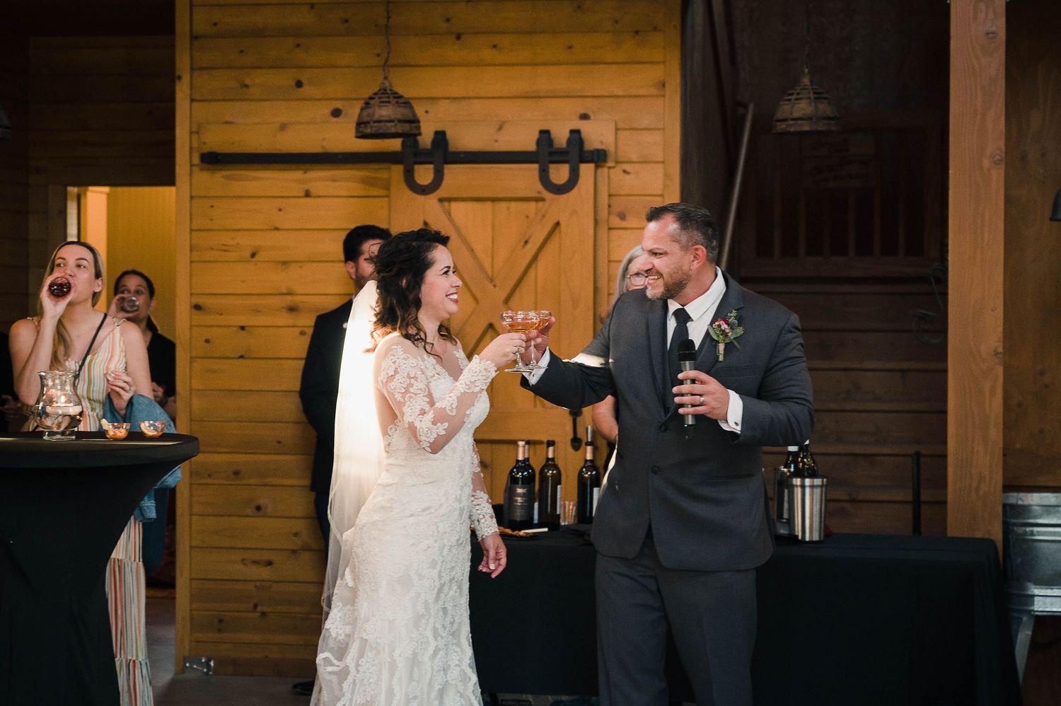 Wedding celebration in rustic barn venue with couple enjoying drinks and laughter.