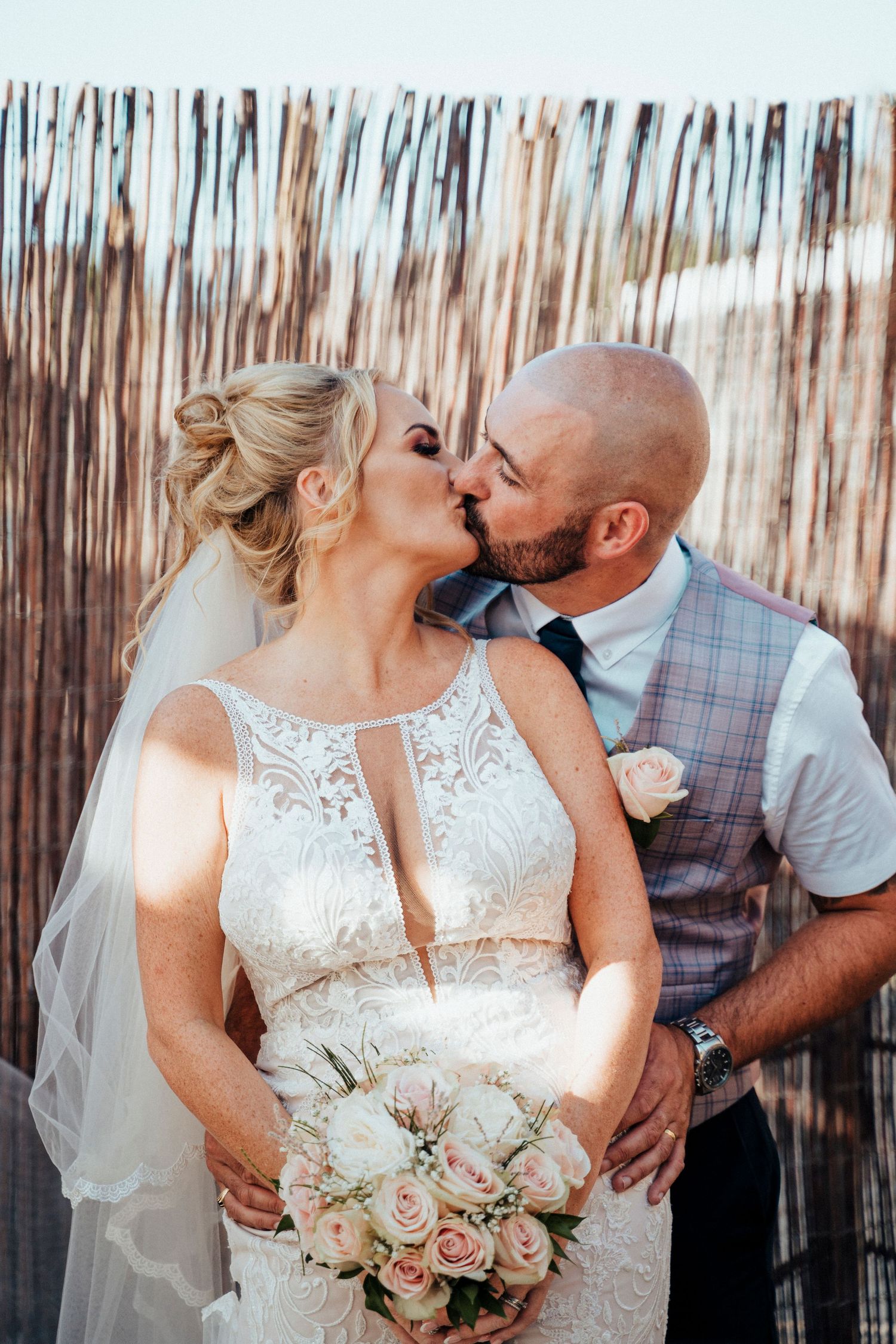 Intimate wedding portrait with couple sharing romantic moment against rustic bamboo backdrop.