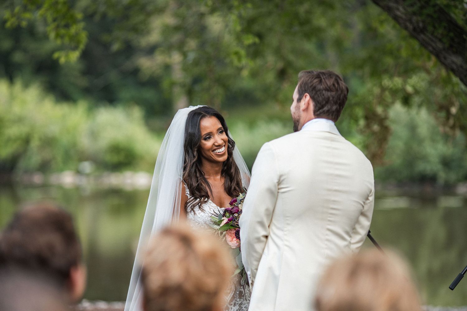 An outdoor wedding ceremony by a lake with guests watching the happy couple exchange vows.