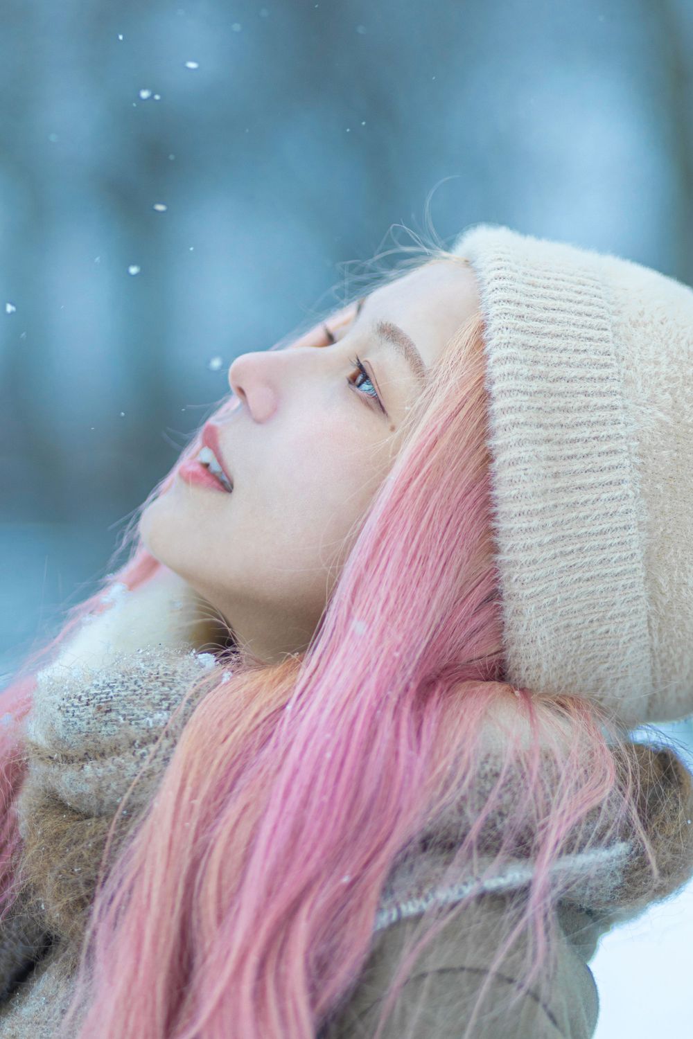 Ethereal winter portrait with white knit hat and pink hair against snowy backdrop.
