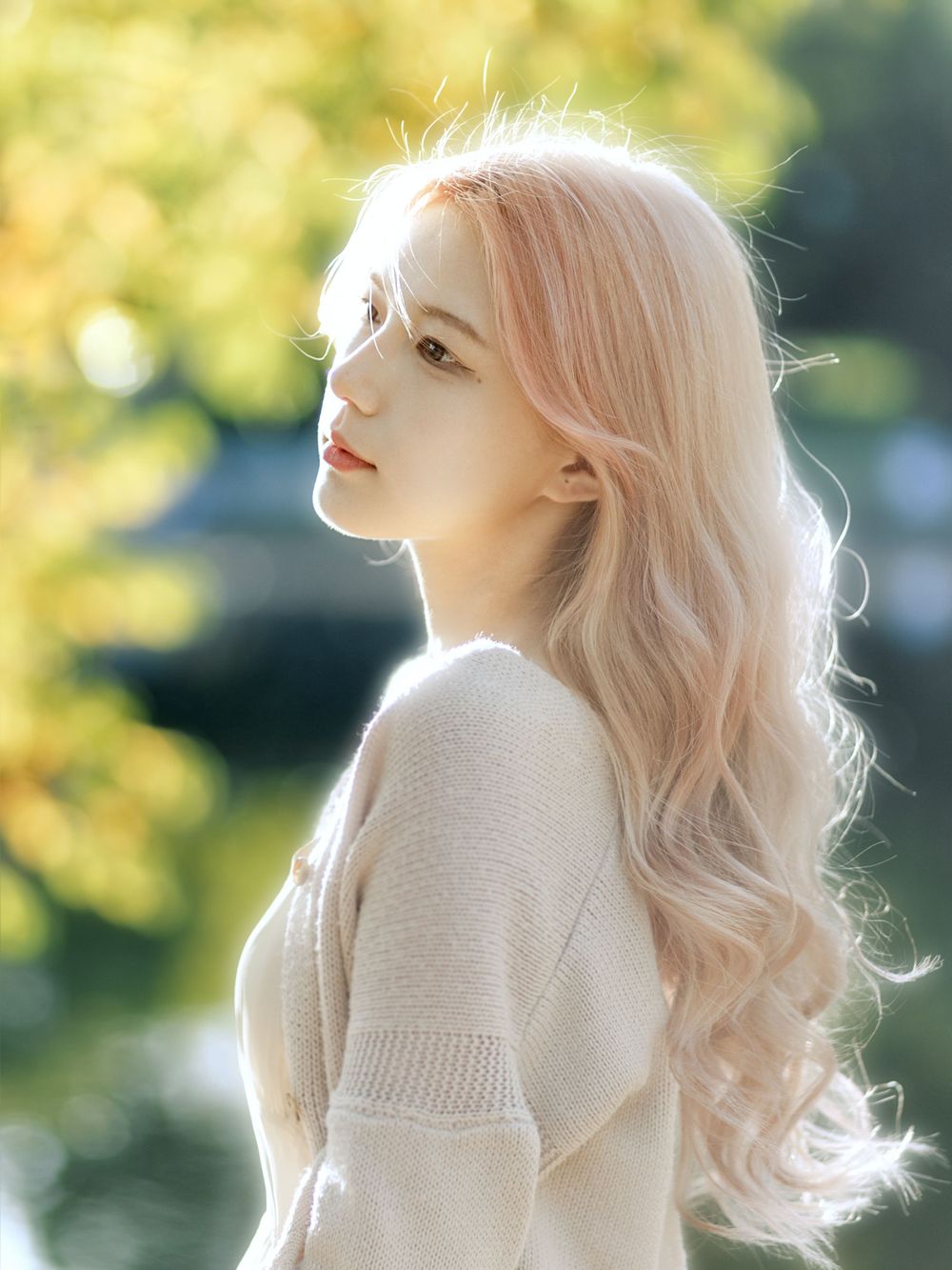 Dreamy portrait of person with light blonde hair in cream sweater against sunny nature backdrop.