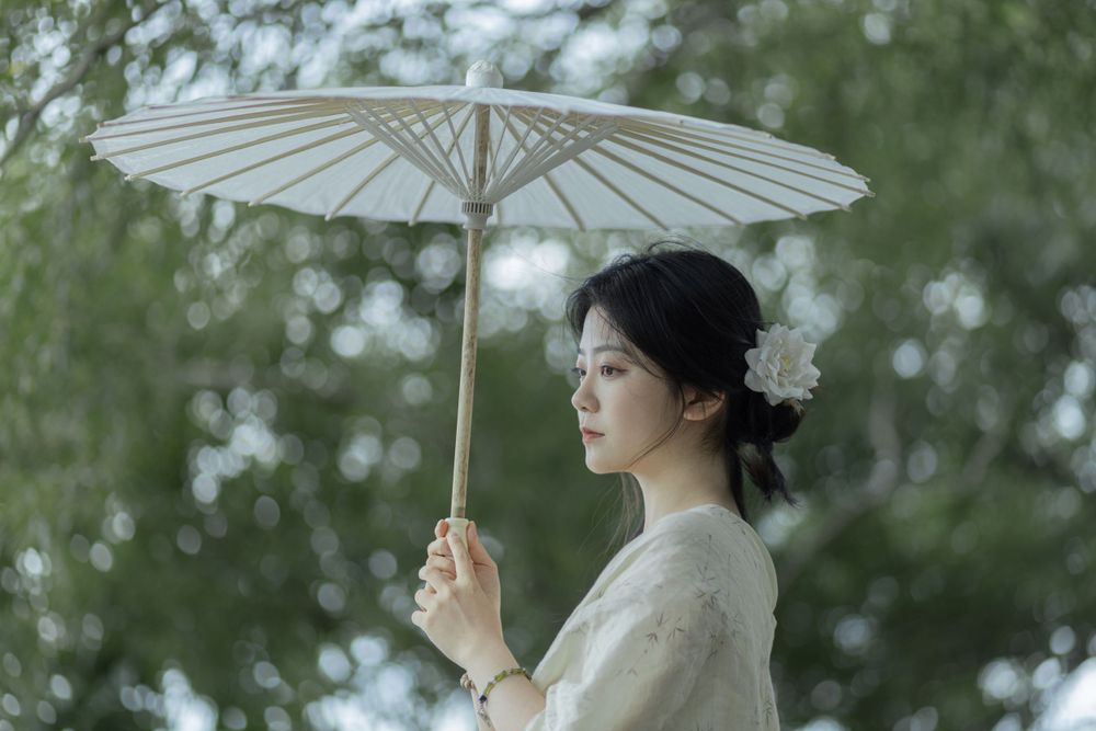 Elegant portrait with traditional paper parasol against soft green natural background.