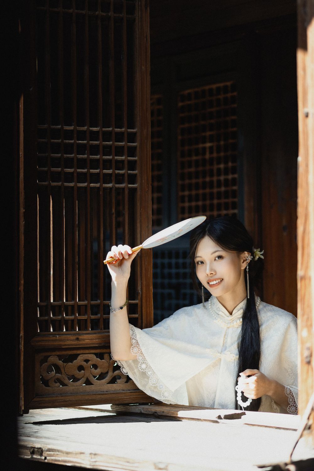 Traditional scene at wooden window with figure holding calligraphy brush in white attire.