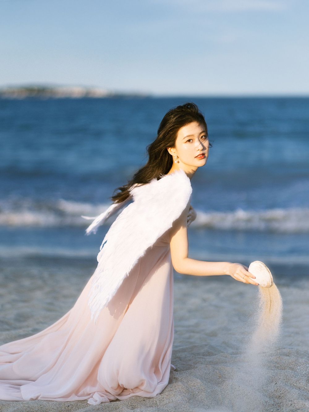 Flowing white dress billows in ocean breeze during sunset beach photoshoot.