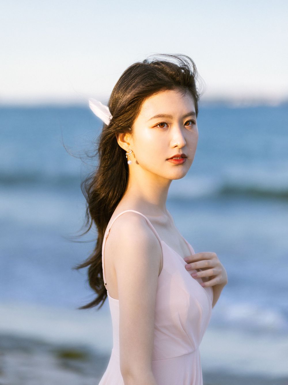 Ethereal beach photoshoot with flowing pink dress against ocean waves.