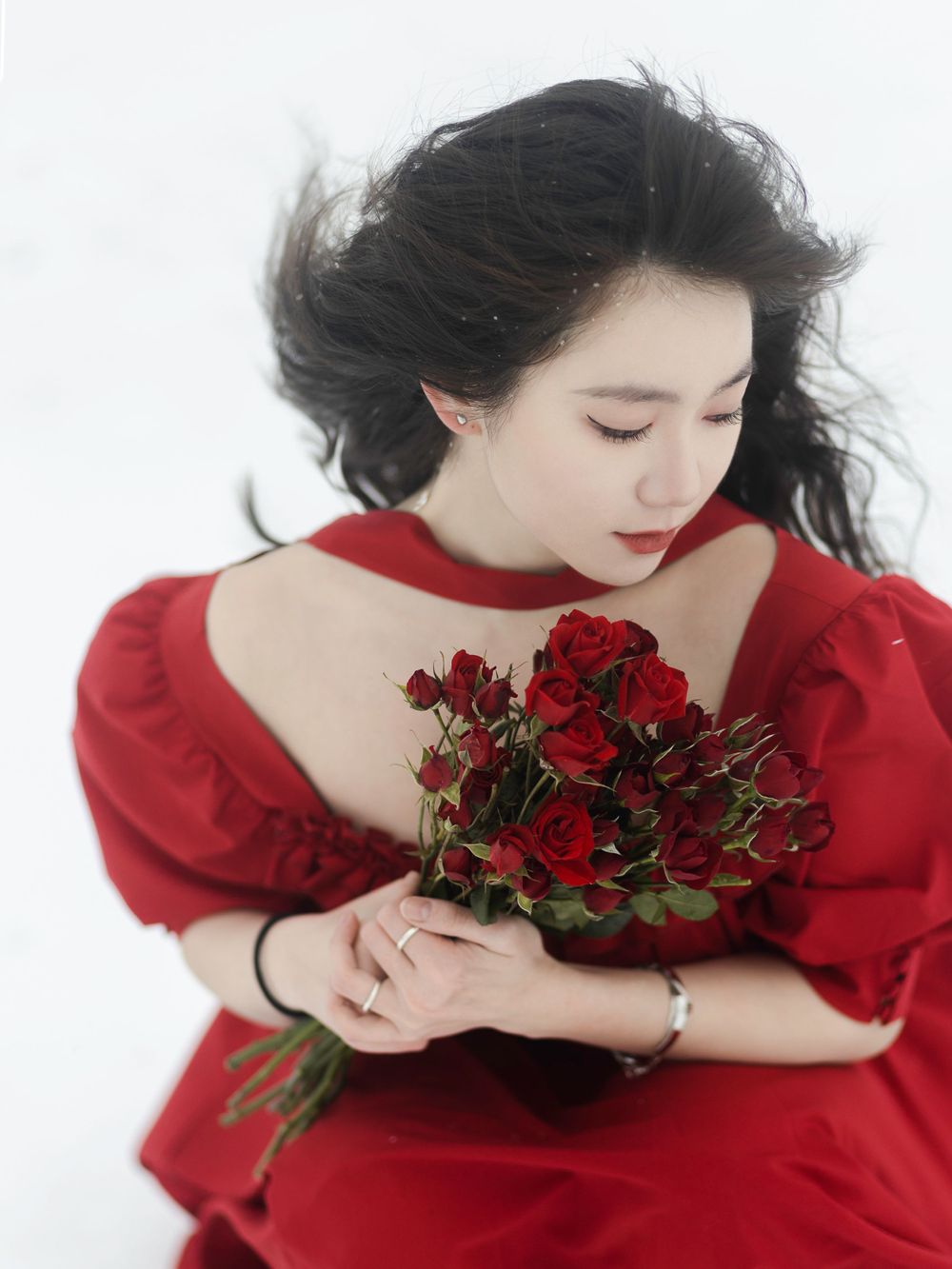 A dramatic winter portrait featuring a red dress and bouquet of deep red roses against pure white snow.