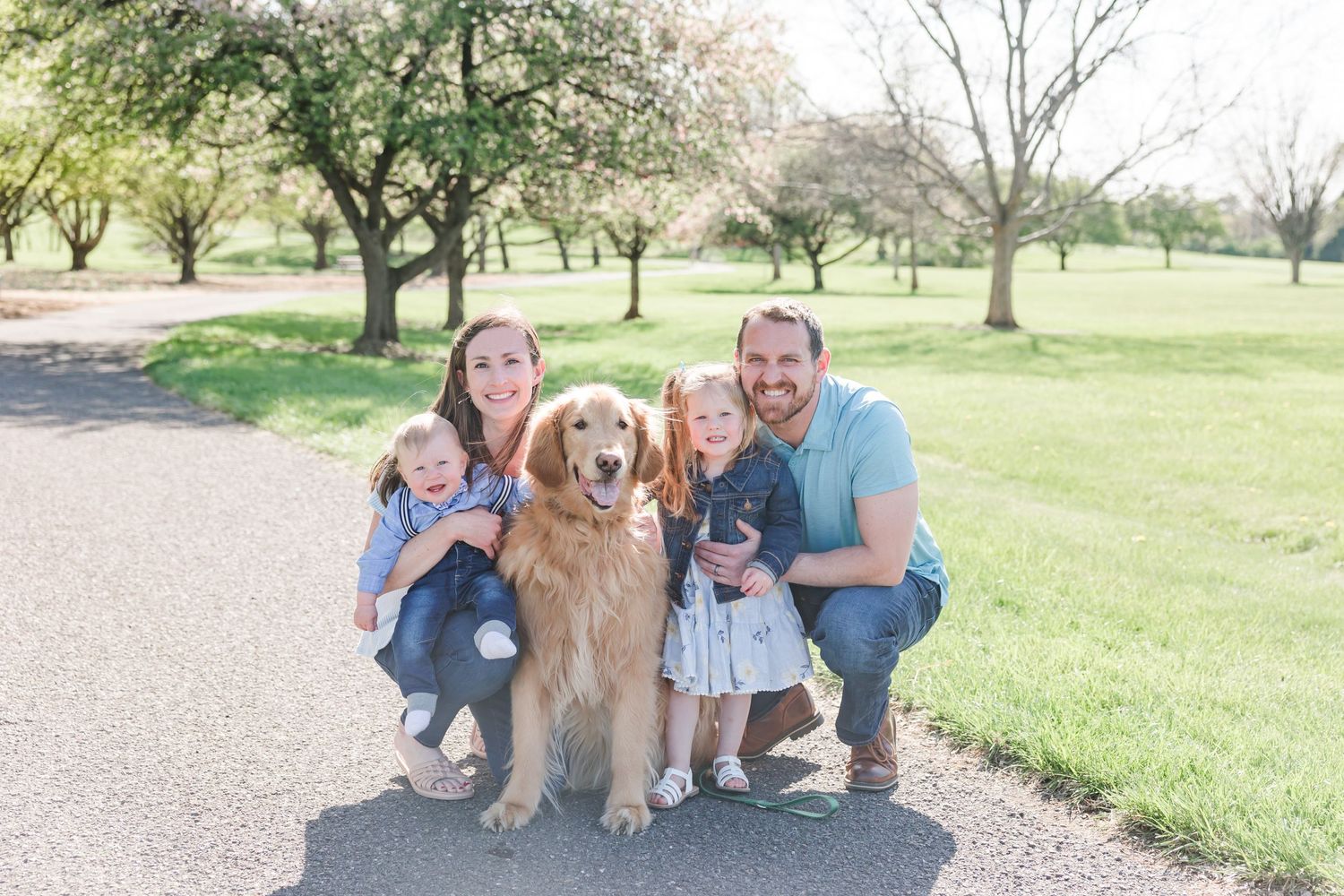 Family group with golden retriever poses together on path in park setting.