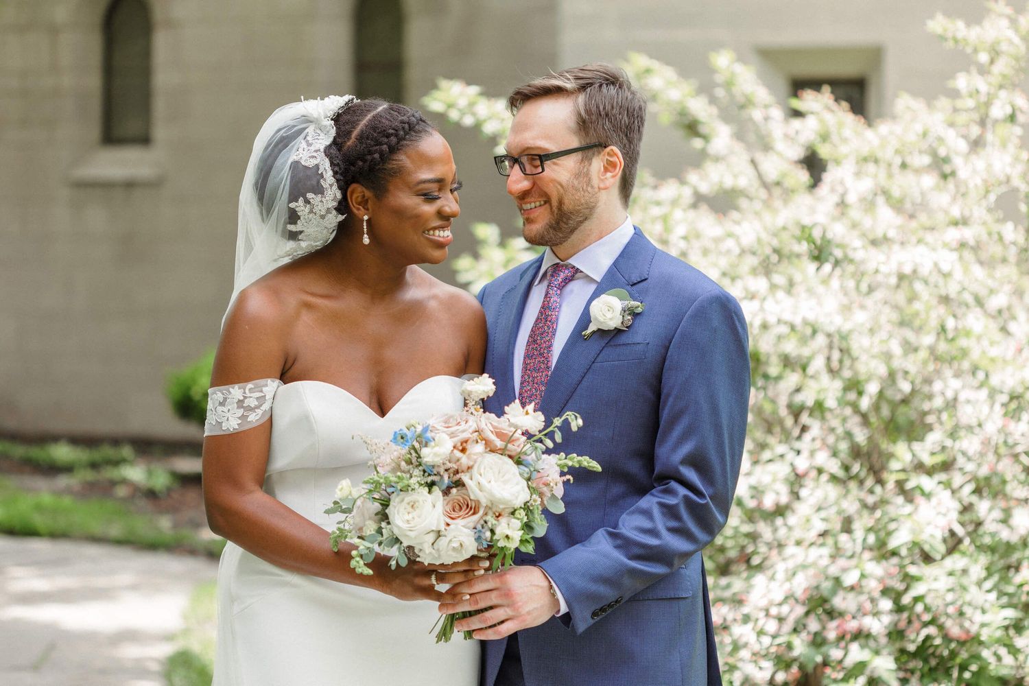A wedding couple poses outdoors with spring blossoms and a pastel bouquet.
