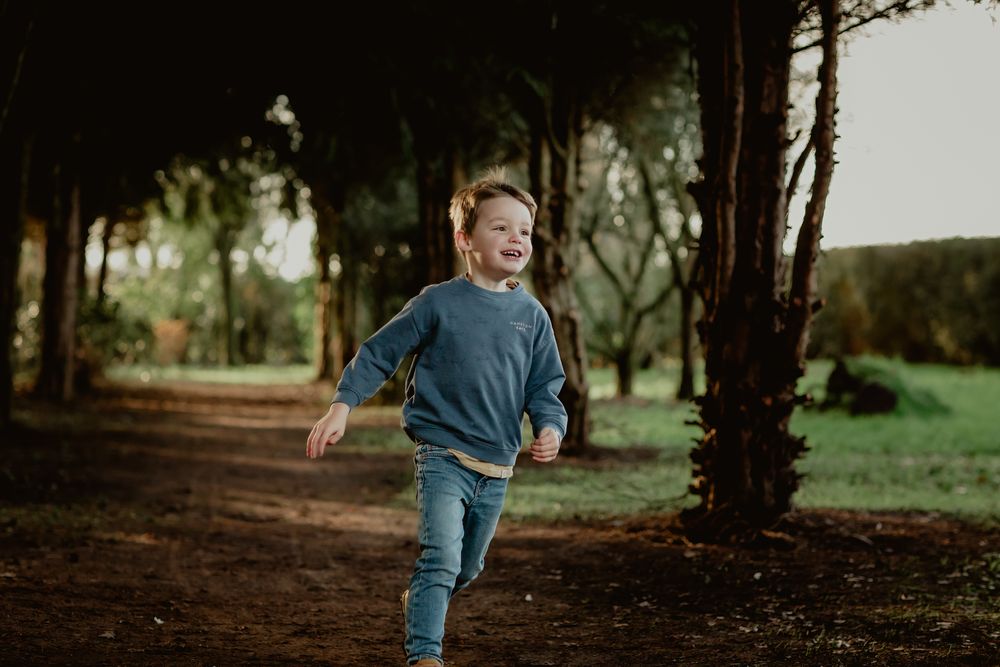 Child running joyfully along a tree-lined dirt path in the forest.