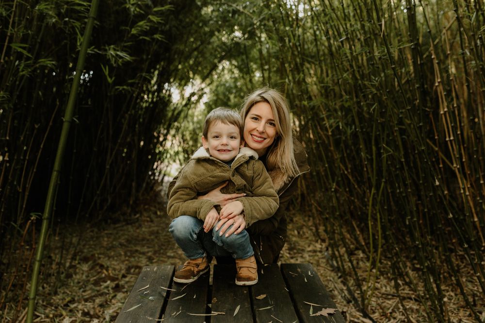 Mother and child sitting together on wooden boardwalk surrounded by bamboo grove.