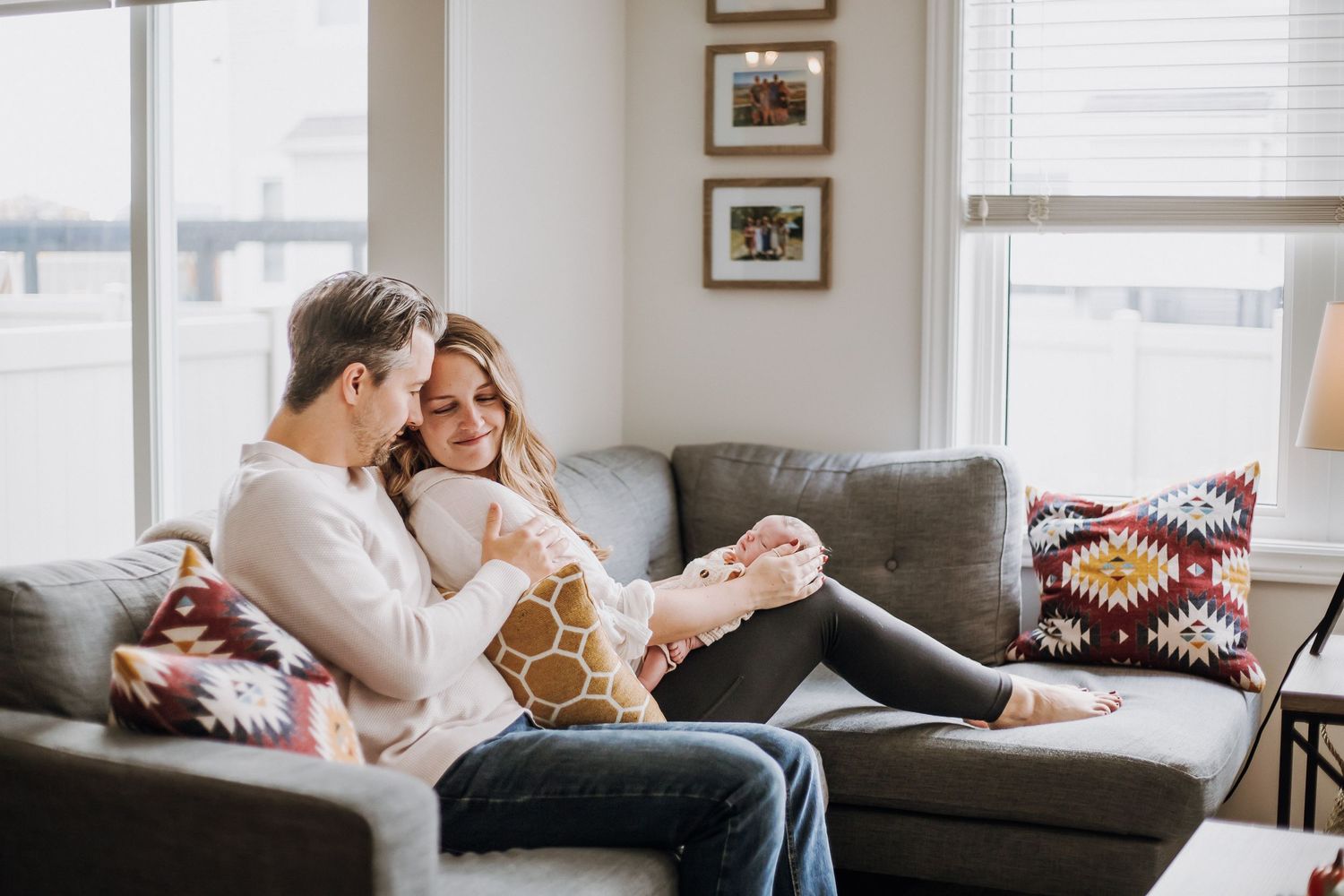 Cozy couple relaxing together on grey sectional sofa with decorative throw pillows in bright living room.