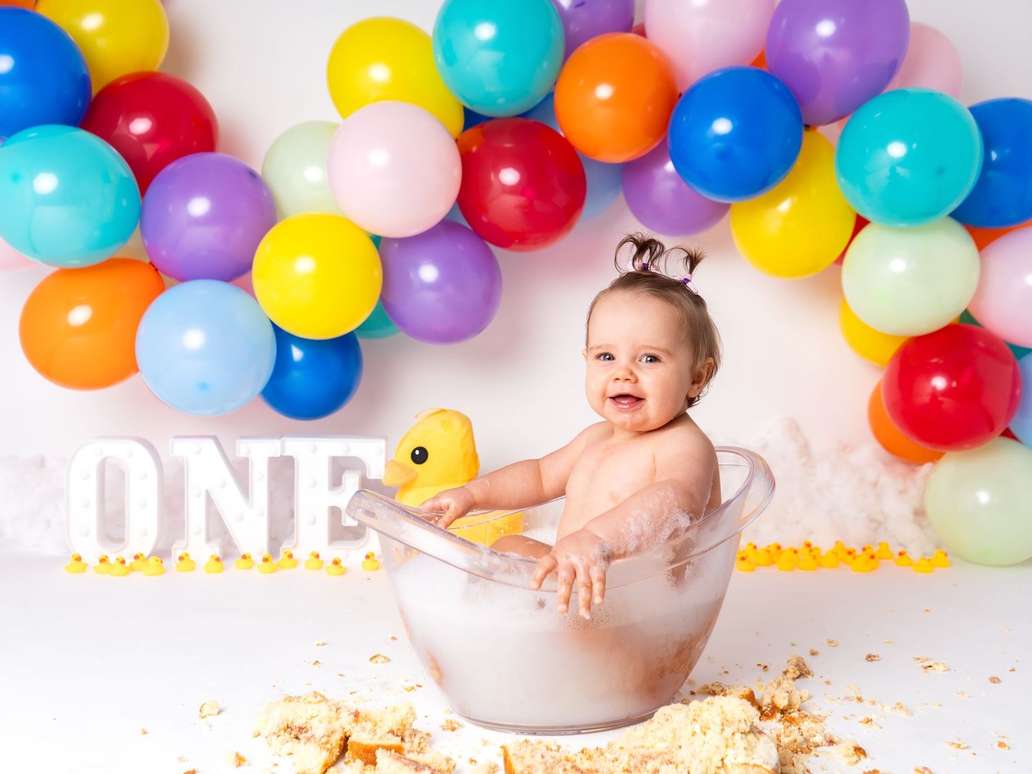 colourful rainbow balloons first birthday one year old girl in bath tub with cake smash photographer in Doncaster.