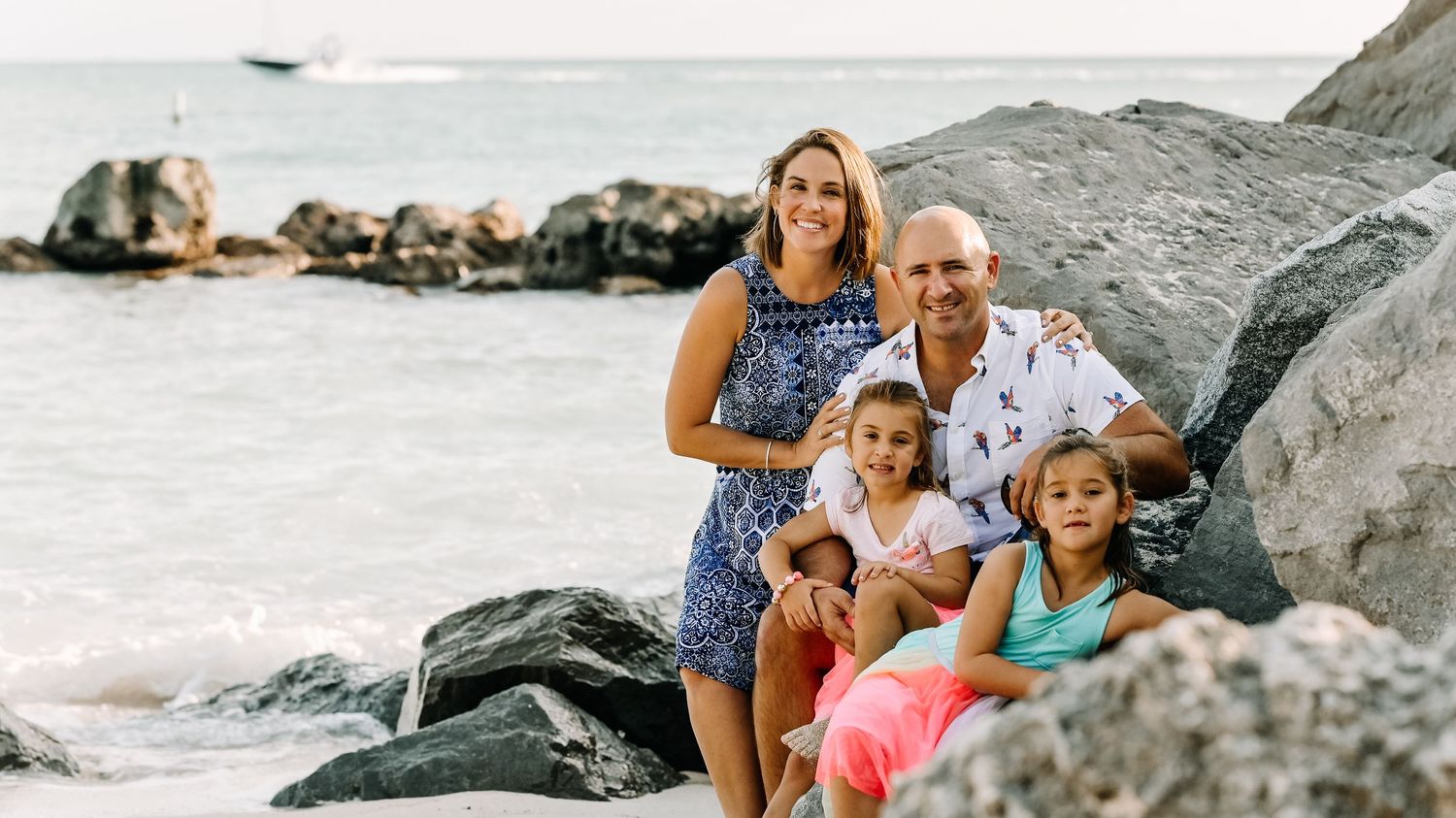 Family poses together on rocky beach with ocean and mountains in background.