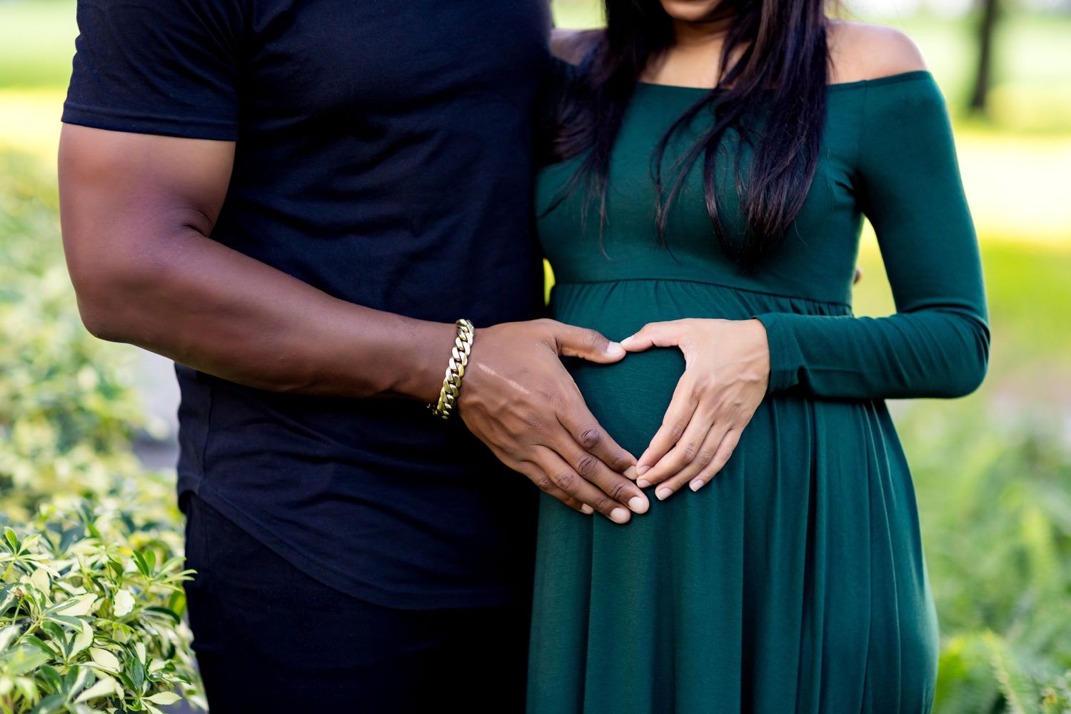 Couple forms heart shape with hands over pregnant belly in maternity photo.