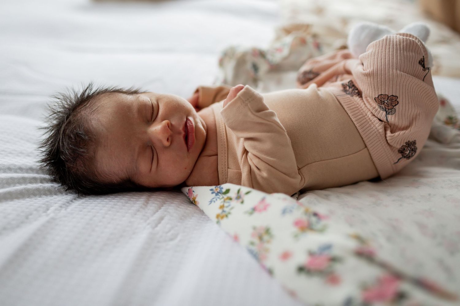 Newborn baby sleeping peacefully in a beige onesie with paw print pattern on white bedding.