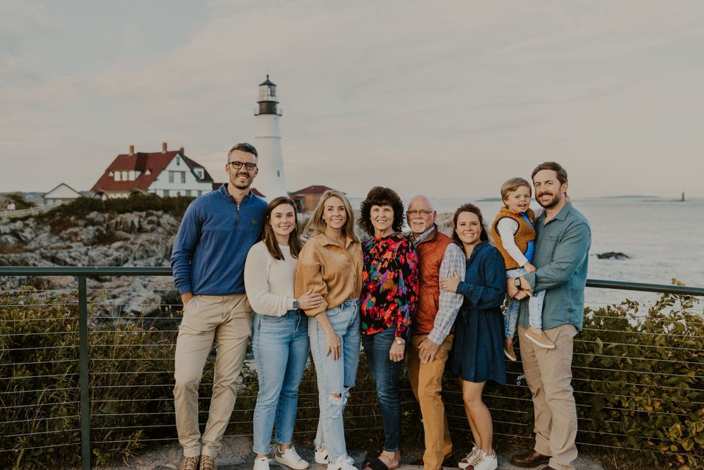 Family group posing together in front of Portland Head lighthouse on a cloudy day.
