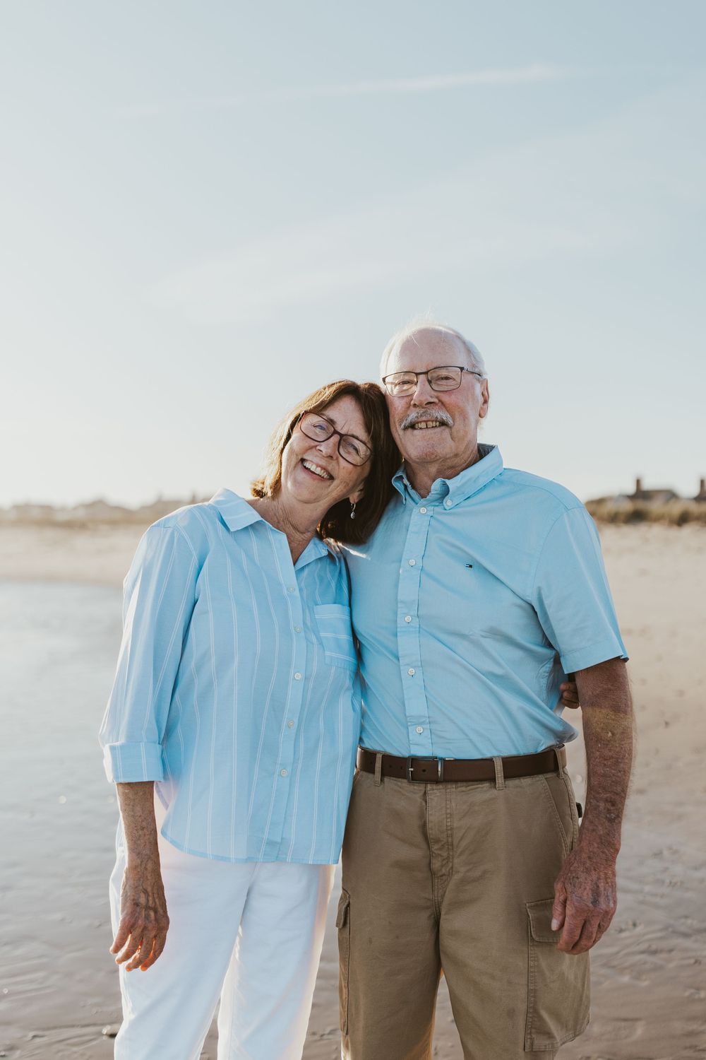 Mature couple in matching blue shirts smiling together on a sunny beach.