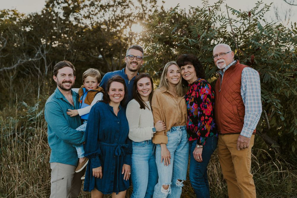 Extended family group portrait in casual clothing against natural foliage background at sunset.