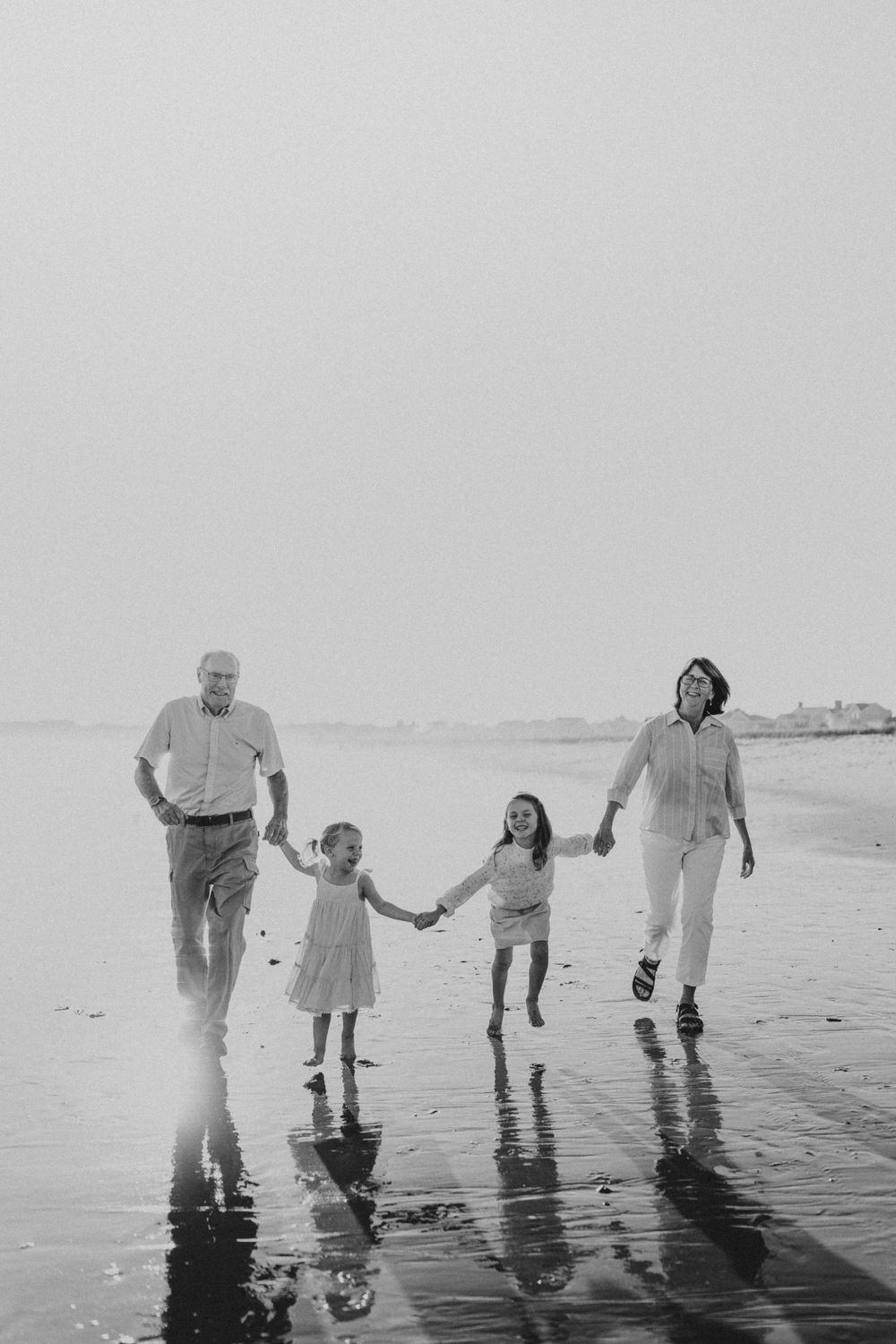 Family of four holding hands while walking along the shoreline at sunset.