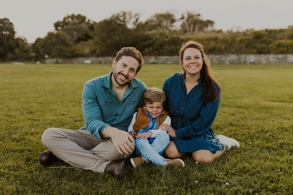 Family sits together on green grass field during golden hour photo session.