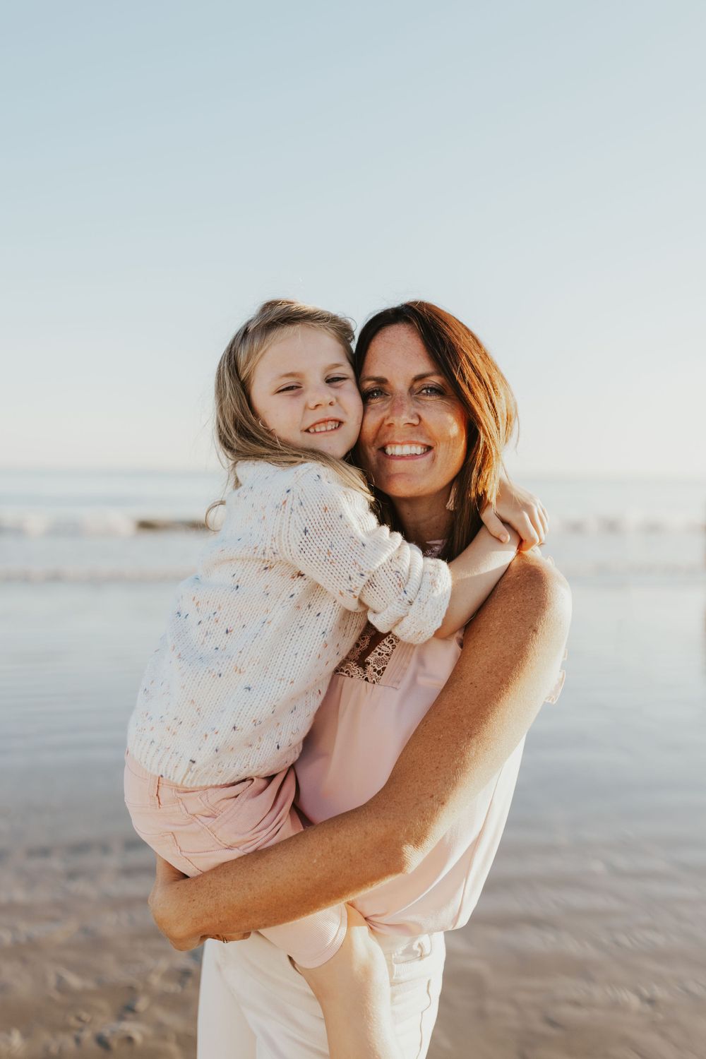 Mother and daughter sharing a joyful embrace on the beach at golden hour.