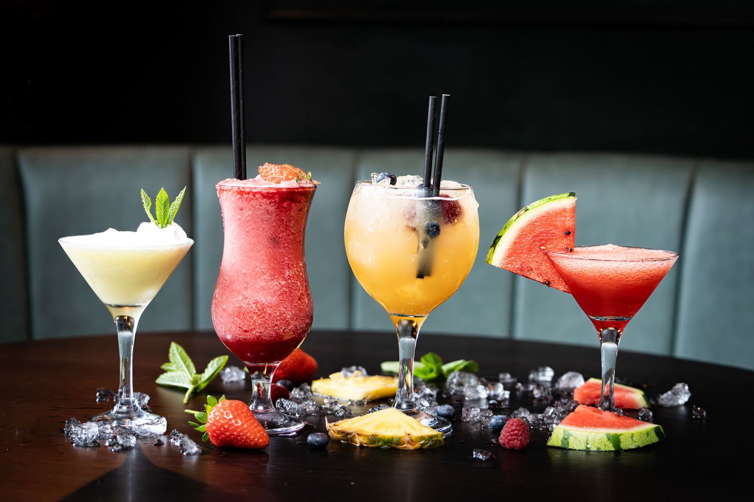 Colorful craft cocktails garnished with fresh fruit and herbs lined up on a dark bar.