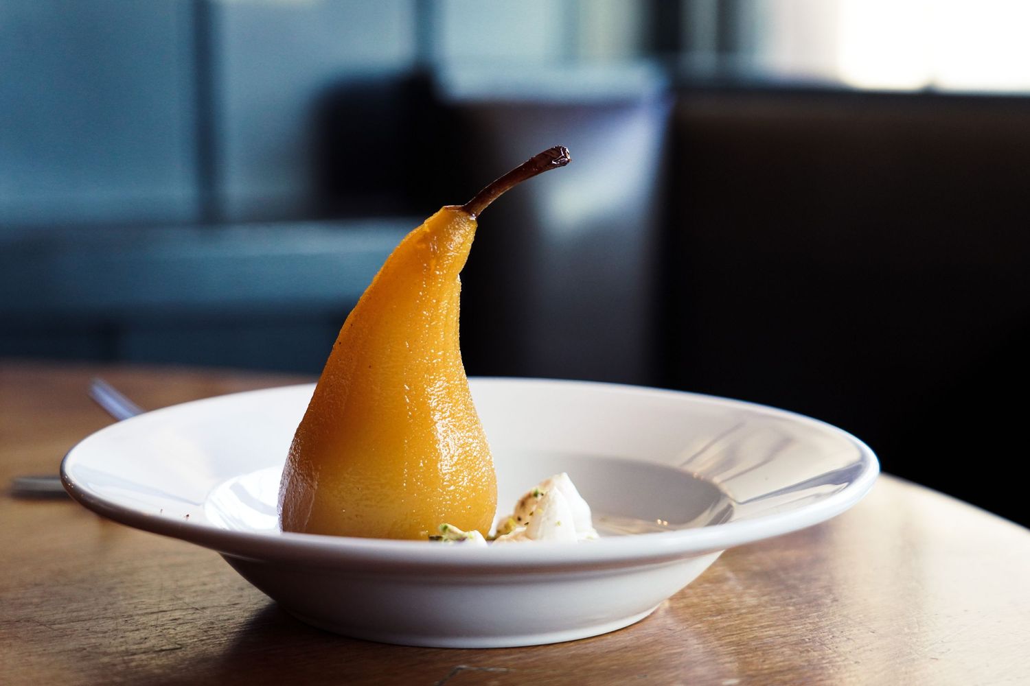 A plated dessert featuring an elegantly poached pear on a white dish with artistic presentation.