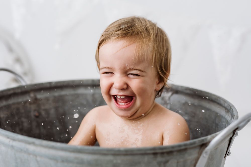 A happy child laughs while sitting in vintage metal wash tub during bath time.