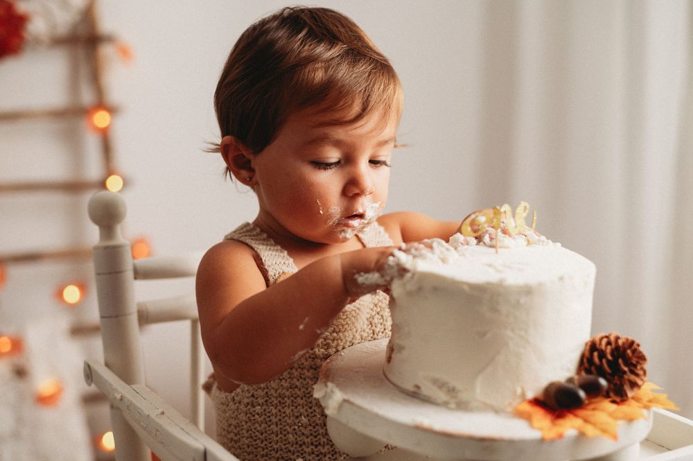 Young child reaching for a white frosted cake in a warm-lit setting.